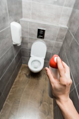 Modern tuvaletteki gri fayanslı oda spreyini tutan adam manzarası.