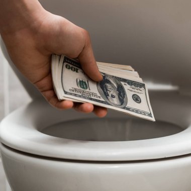 Modern tuvaletteki gri fayanslı klozetin yanında dolar banknotları tutan adam manzarası.