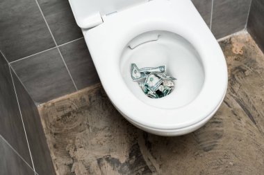 dollar banknotes in toilet bowl in modern restroom with grey tile clipart