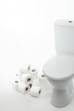 Beyaz arka planda tuvalet kağıdı ruloları olan seramik temiz klozet.