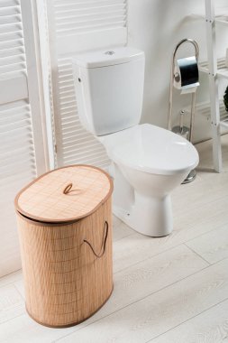 Beyaz modern tuvaletin içi. Tuvalet kapağı katlı. Çamaşır sepeti, tuvalet fırçası.