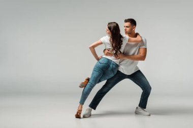 Gri arkaplanda dans eden tişörtlü ve kot pantolonlu dansçılar 