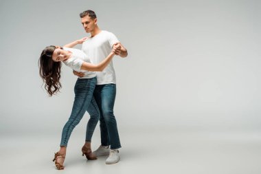 Gri arkaplanda dans eden tişörtlü ve kot pantolonlu dansçılar 