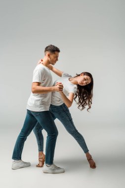 Gri arkaplanda dans eden tişörtlü ve kot pantolonlu dansçılar 