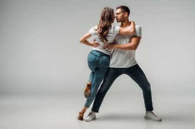 Gri arkaplanda dans eden tişörtlü ve kot pantolonlu dansçılar 