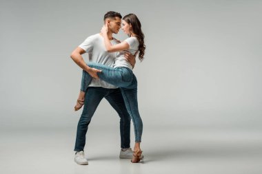 Gri arkaplanda dans eden tişörtlü ve kot pantolonlu dansçılar 