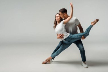Gri arkaplanda dans eden tişörtlü ve kot pantolonlu dansçılar 