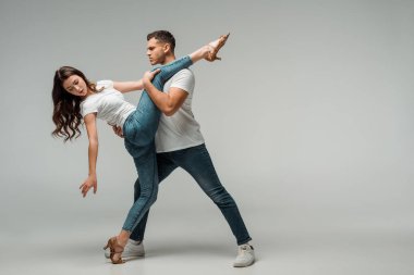 Gri arkaplanda dans eden tişörtlü ve kot pantolonlu dansçılar 
