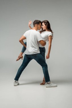 Gri arkaplanda dans eden tişörtlü ve kot pantolonlu dansçılar 