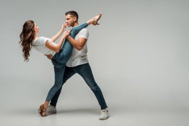 Gri arkaplanda dans eden tişörtlü ve kot pantolonlu dansçılar 