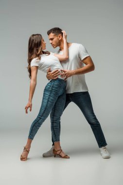 Gri arkaplanda dans eden tişörtlü ve kot pantolonlu dansçılar 