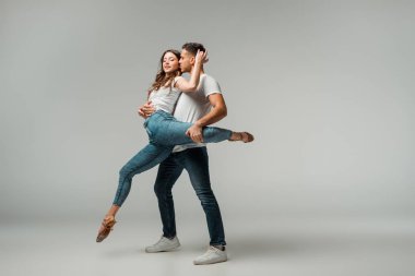 Gülümseyen dansçılar tişört ve kot pantolon giyip gri arka planda dans ediyorlar. 