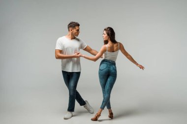 Gri arka planda kot pantolonlu dansçılar dans ediyor. 