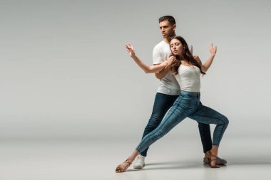 Gri arka planda kot pantolonlu dansçılar dans ediyor. 