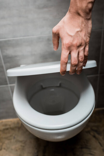 cropped view of man holding toilet lid in modern restroom with grey tile