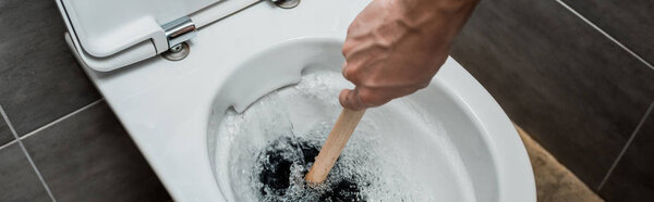 cropped view of plumber using plunger in toilet bowl during flushing in modern restroom with grey tile, panoramic shot