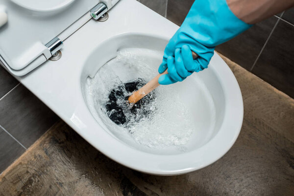 обрезанный вид водопроводчика с помощью вантуза в унитазе во время смыва в современном туалете с серой плиткой
