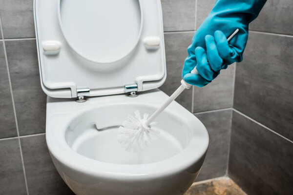 cropped view of cleaner cleaning ceramic toilet bowl with toilet brush in modern restroom with grey tile