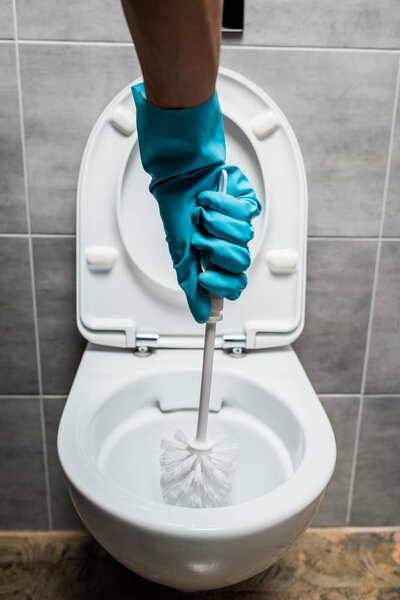cropped view of cleaner cleaning ceramic toilet bowl with toilet brush in modern restroom with grey tile