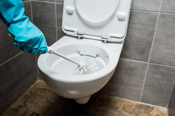 cropped view of cleaner cleaning ceramic toilet bowl with toilet brush in modern restroom with grey tile