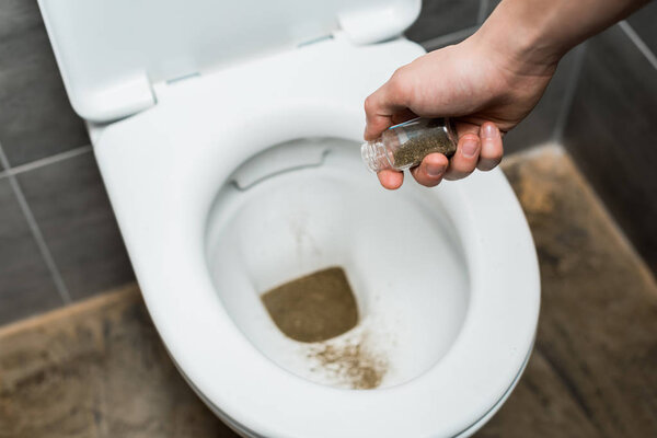cropped view of man throwing away marijuana in toilet bowl
