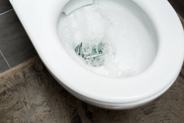 clean white toilet bowl with flushing money in modern restroom with grey tile