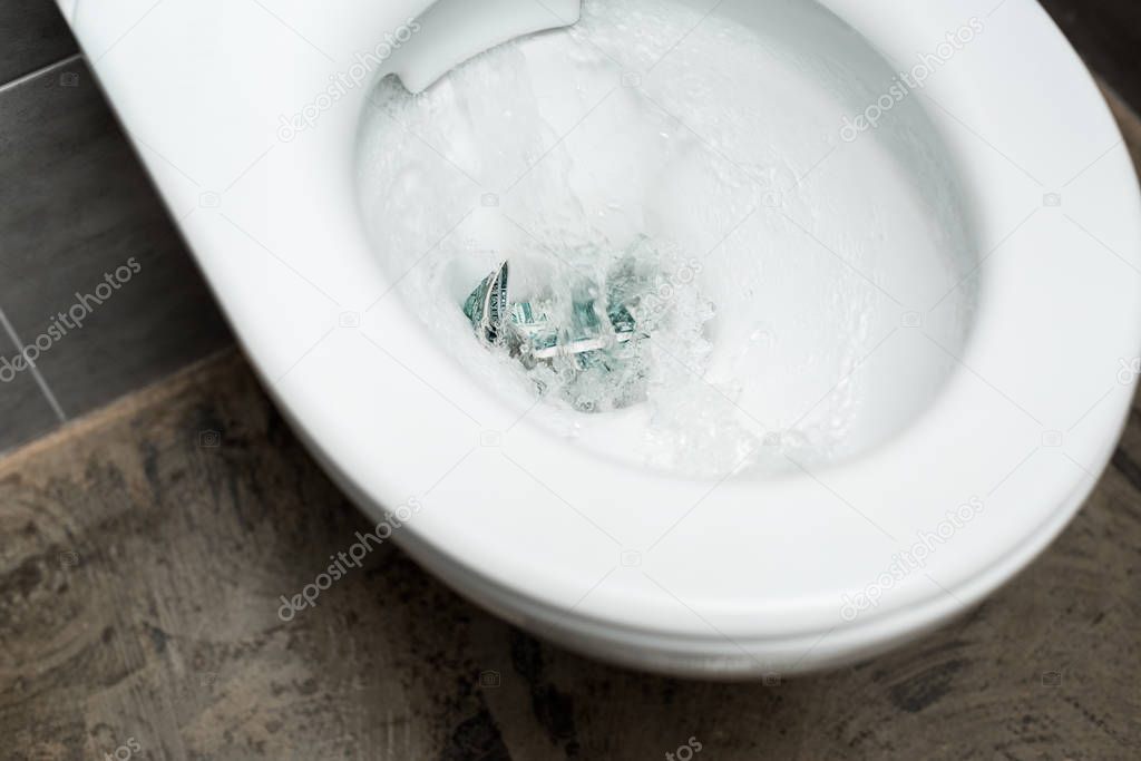 clean white toilet bowl with flushing money in modern restroom with grey tile