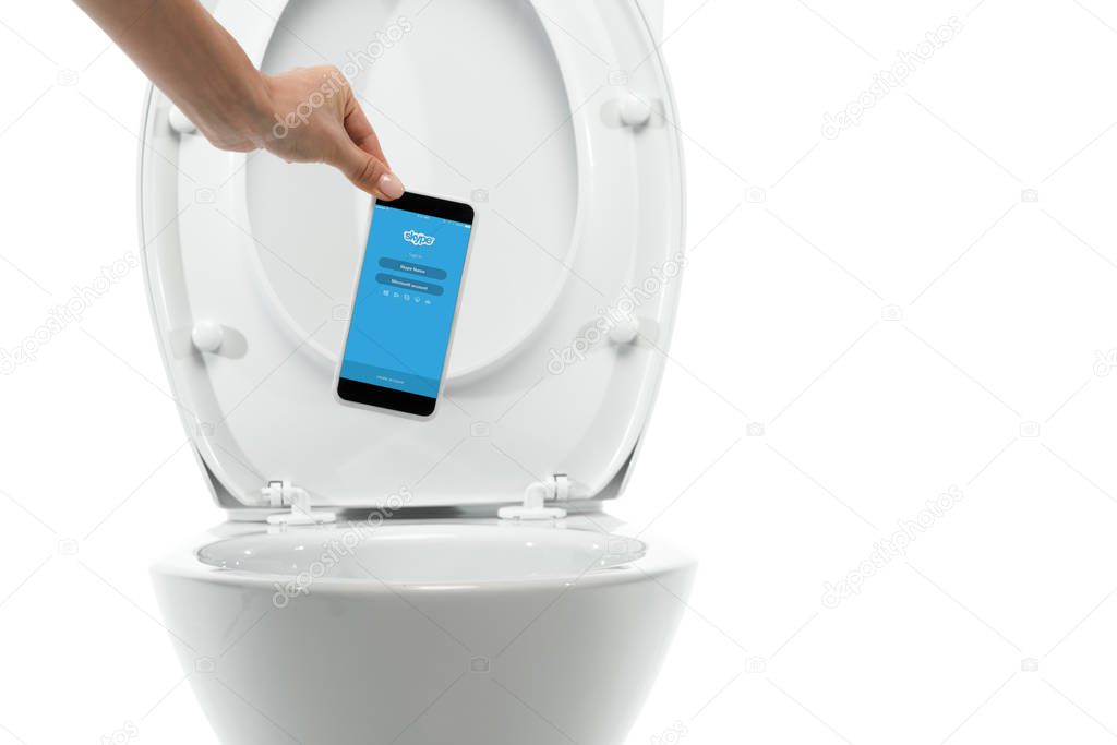 KYIV, UKRAINE - NOVEMBER 7, 2019: cropped view of woman throwing away smartphone with skype app in ceramic clean toilet bowl isolated on white