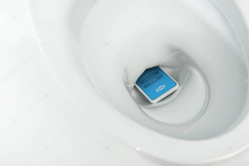 KYIV, UKRAINE - NOVEMBER 7, 2019: close up view of smartphone with skype app in ceramic clean toilet bowl isolated on white