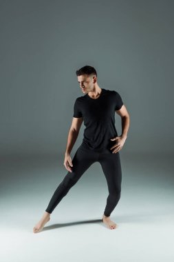 Siyah taytlı yakışıklı dansçı ve siyah arka planda çağdaş tişört dansı yapan.