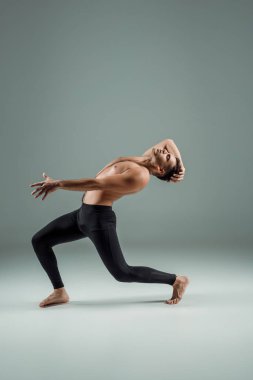 Siyah taytlı yakışıklı dansçının yan görünüşü koyu arkaplanda çağdaş dans ediyor.