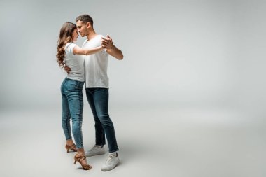 smiling dancers in t-shirts and jeans dancing bachata on grey background  clipart