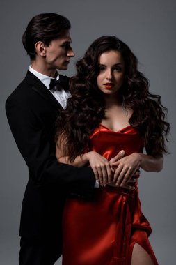 Takım elbiseli romantik bir çift ve gri üzerinde kırmızı ipek elbiseler giyiyor.