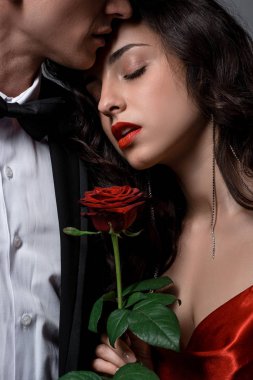 Kırpılmış romantik çiftin kucaklaşması ve kırmızı gül çiçeği tutması 