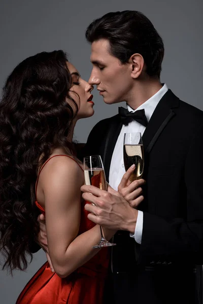 这对浪漫的夫妇举着香槟酒杯要接吻 孤零零地躺在灰色的床上 — 图库照片