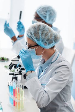 Mikroskop kullanan seçici biyolog ve elinde büyüteç tutan Afrikalı Amerikalı meslektaşı.