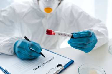 cropped view of scientist writing and holding test tube with lettering dna test  clipart