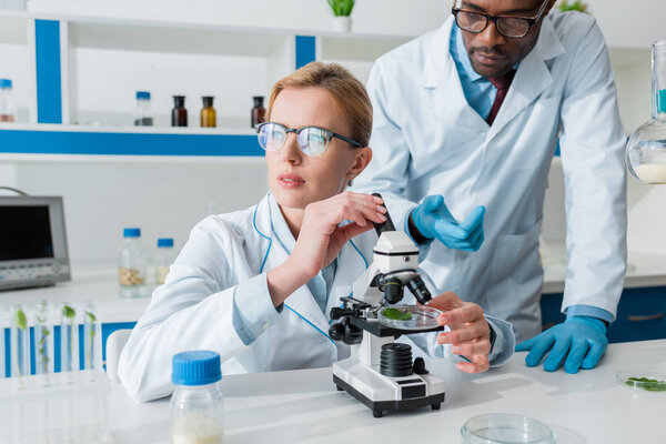 поликультурные биологи в белых халатах используют микроскоп в лаборатории
 
