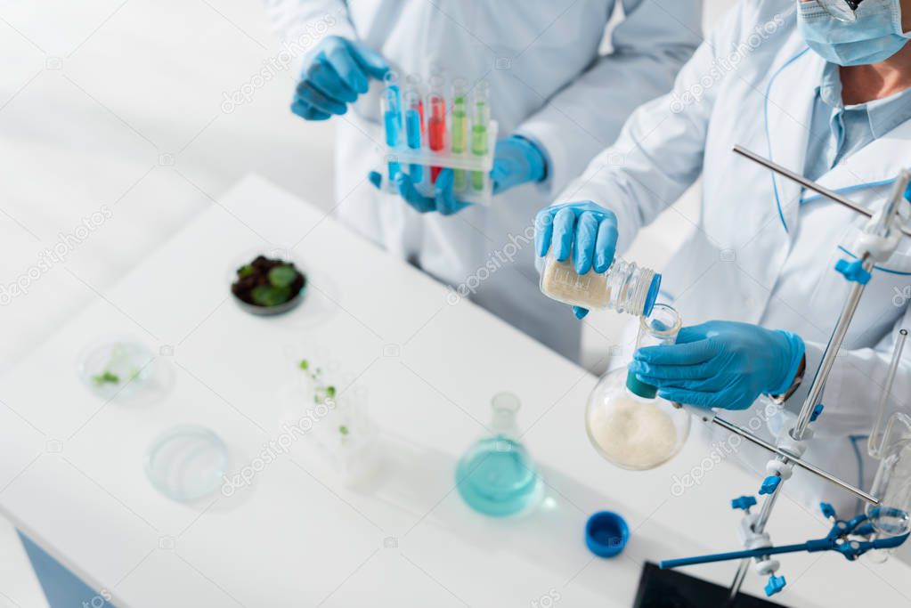 cropped view of biologists in white coats doing test in lab  