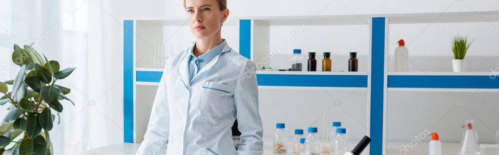 panoramic shot of biologist in white coat looking away in lab 