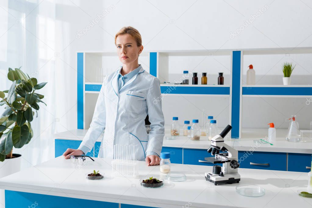 attractive biologist in white coat looking away in lab 