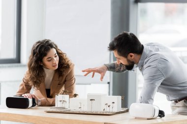 Gülümseyen sanal gerçeklik mimarları konuşuyor ve ev modeline bakıyor. 