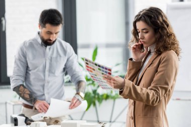 Renklerin düzenine bakan sanal gerçeklik mimarının seçici odak noktası ve elinde kağıt tutan meslektaşı 