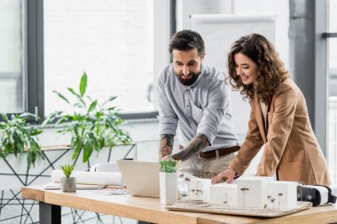 smiling virtual reality architects looking at laptop in office  clipart