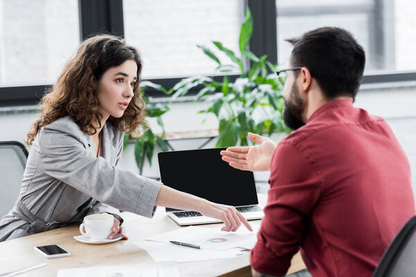 account manager pointing with finger at papers and her colleague pointing with hand at laptop 