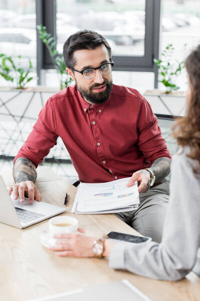 selective focus of account manager holding papers and talking with colleague 