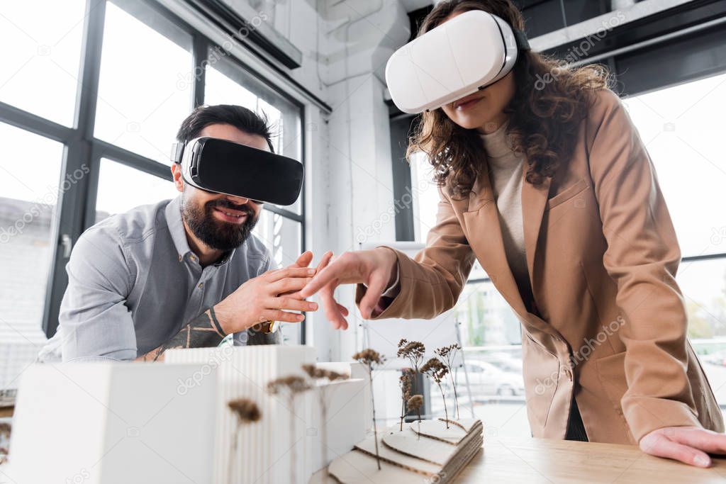 virtual reality architects in virtual reality headsets pointing with finger at model of house  