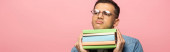 Skeptický muž s knihami odvrácenými na růžovém, panoramatickém záběru