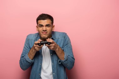 Kyiv, Ukrayna - 12 Kasım 2019: Pembe arka planda suratını buruşturan joystick 'li genç adam