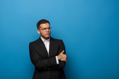 Sceptical businessman with crossed arms looking away on blue background clipart